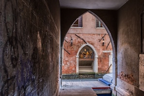 An arched passageway with a rustic brick wall, a wooden bench, and a small table with a sign. - Rialto Bridge Venetian Style (Venice)