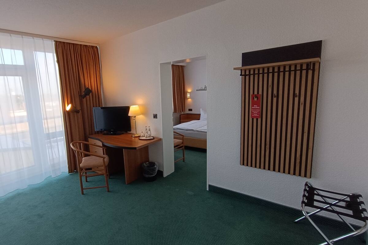 Et hotelværelse med skrivebord, stol, seng og udsigt gennem vinduet.