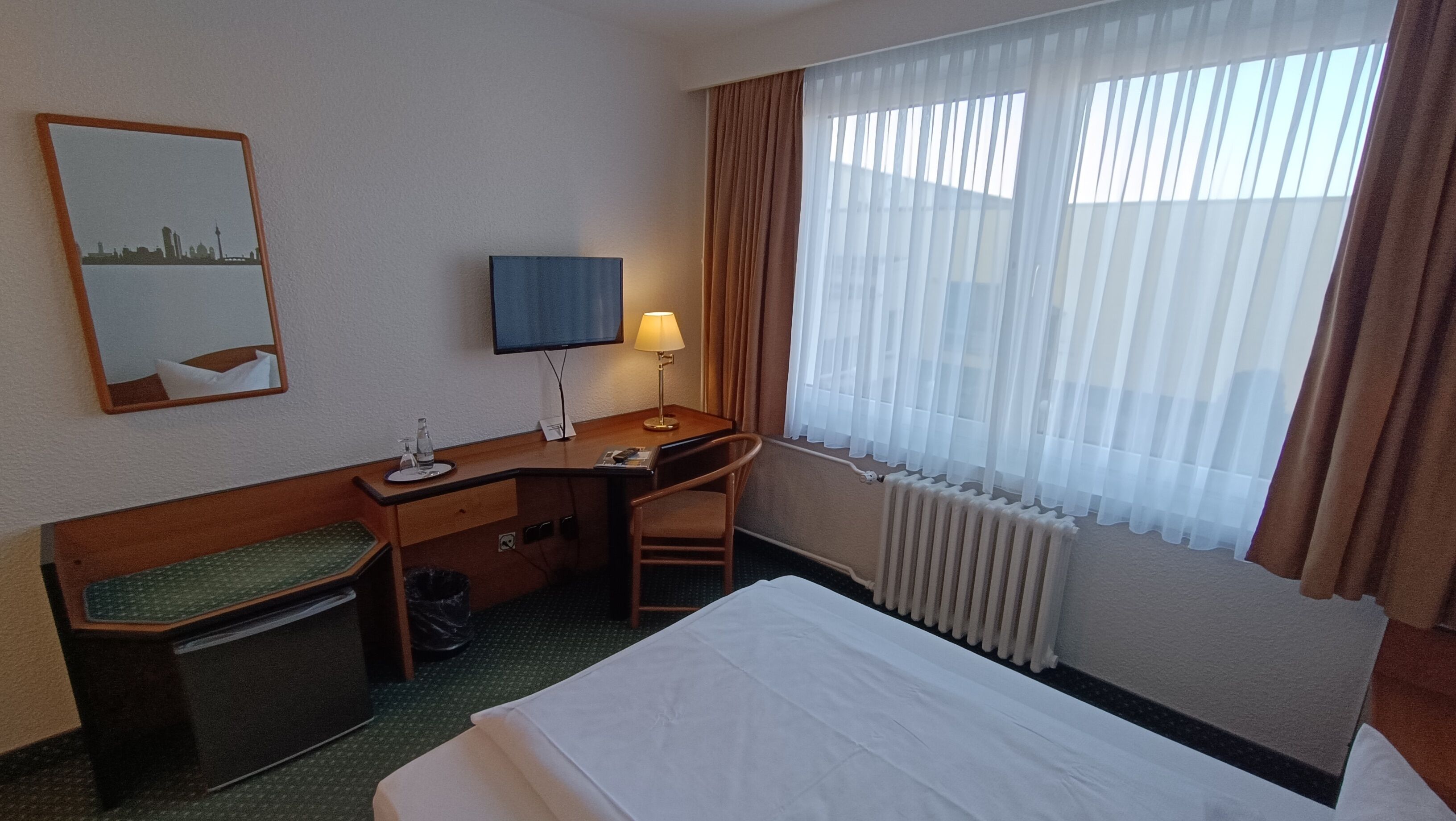 A hotel room with a bed, desk, chair, and a window with curtains.