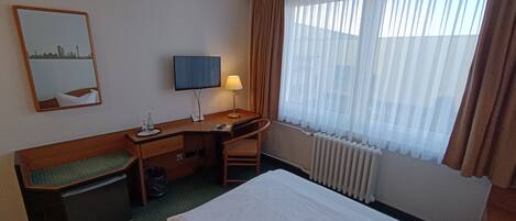 A hotel room with a bed, desk, chair, and a window with curtains.