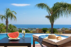 A poolside lounge with a view of the sea, a slice of watermelon, and a glass of water on a table.