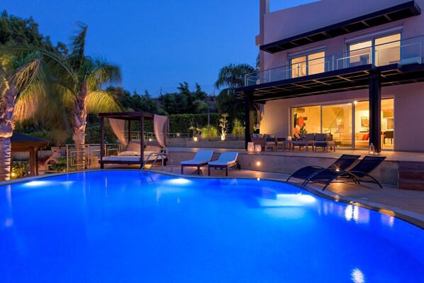 A swimming pool with lounge chairs, a covered seating area, and a building with large windows.