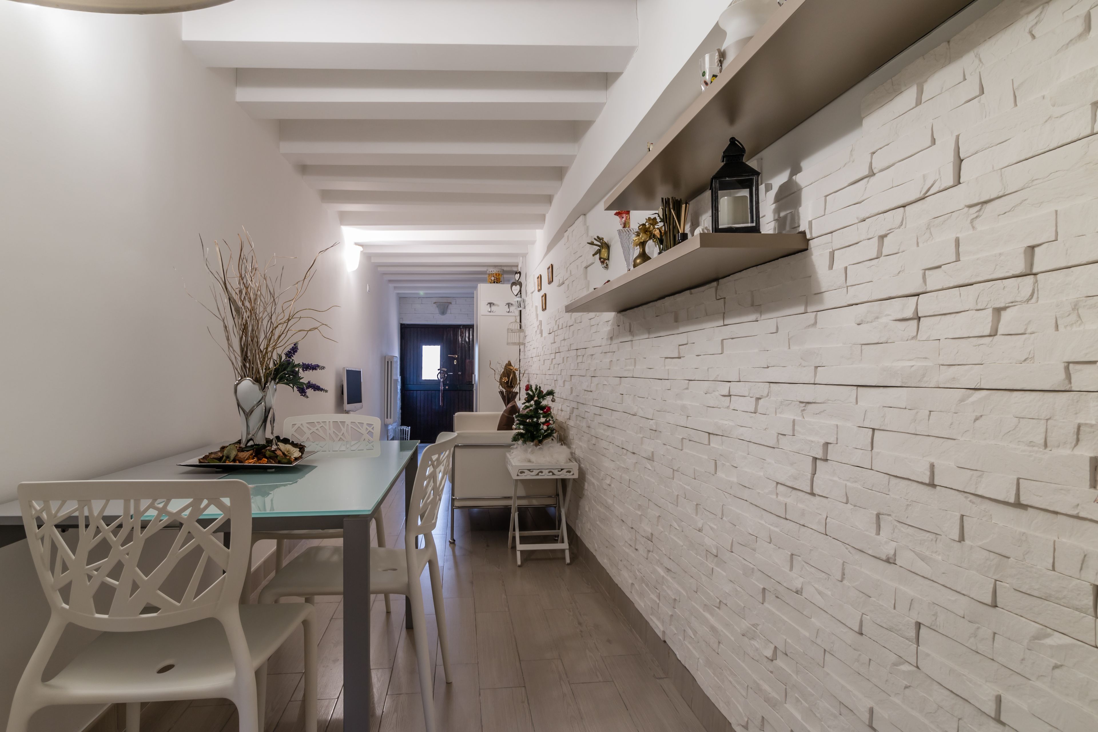A modern dining area with a glass table, white chairs, and a brick wall.