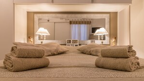 A hotel room with a large mirror, two bedside lamps, a bed with a patterned bedspread, and two rolled towels on the floor. - Cà Lessia (Venice)