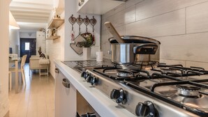 A modern kitchen with a stainless steel stove, white cabinetry, and a wooden dining table with chairs. - Cà Lessia (Venice)