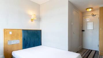 Habitació d'hotel amb un llit, una làmpada penjada a la paret, una porta amb un senyal i una catifes amb ratlles.