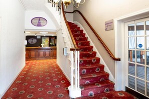 En hotellobby med et rødt tæppe og en trappe op til receptionen.