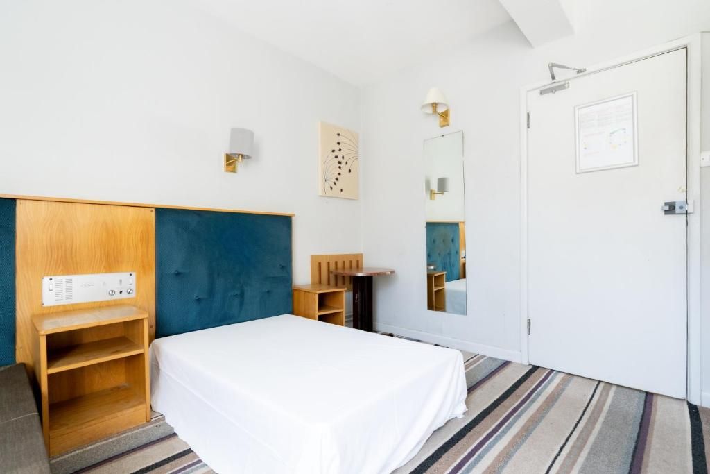 Quarto de hotel com cama, guarda-roupa de madeira, escrivaninha, espelho e luminária na parede.
