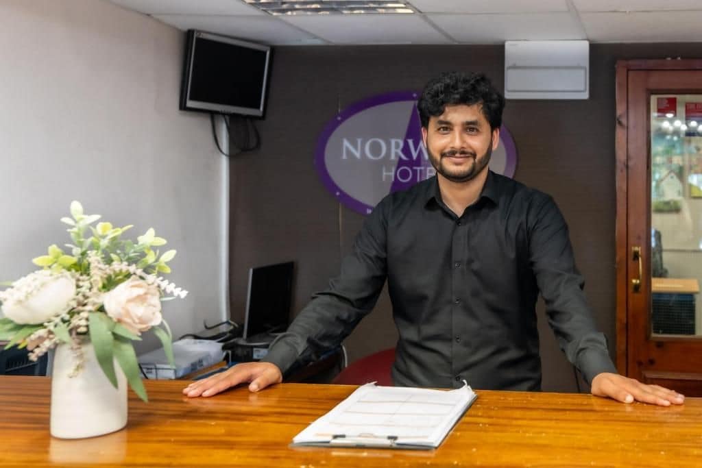 Mostrador de recepción de hotel con un arreglo floral, un monitor y un letrero que dice 'NORW HOTEL'.
