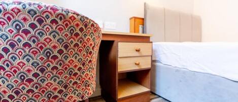 Una habitación de hotel con una cama, una mesita de noche de madera con cajones y una silla estampada.