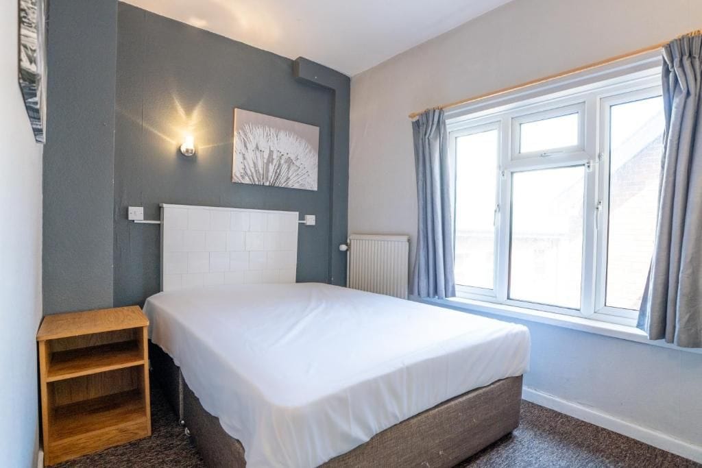 Ein Schlafzimmer mit Bett, Nachttisch, Heizkörper und einem Vorhangfenster.