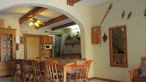 A dining area with a large wooden table and chairs, wooden cabinets, and a ceiling fan. - Happy & Healthy Farmhouse Gozo (Gharb)