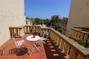 A small outdoor patio with a round table and two chairs, a wooden railing, and a view of the sea and palm trees in the background. - Happy & Healthy Farmhouse Gozo (Gharb)