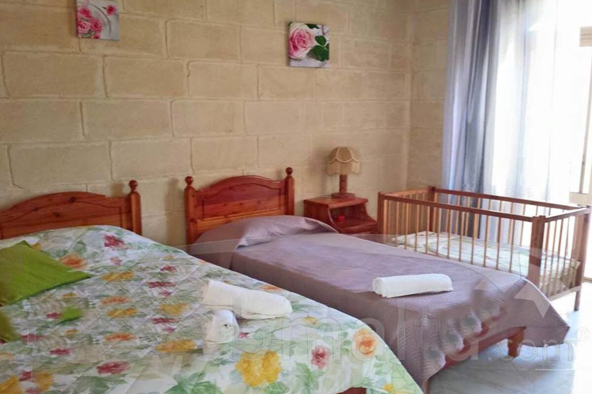 Une chambre avec deux lits, un berceau en bois, une table de chevet et une fenêtre avec des rideaux.