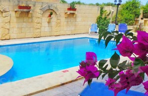 A swimming pool with stone walls and a few lounge chairs. - Happy & Healthy Farmhouse Gozo (Gharb)