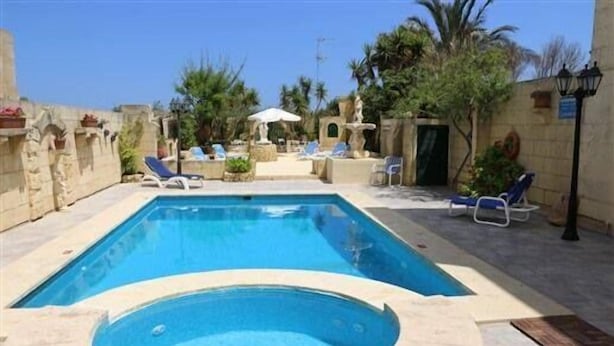 A rectangular swimming pool with a hot tub in the center, surrounded by lounge chairs and umbrellas. - Happy & Healthy Farmhouse Gozo (Gharb)