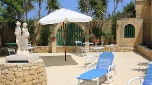 A pool area with lounge chairs, a statue, and a stone wall. - Happy & Healthy Farmhouse Gozo (Gharb)