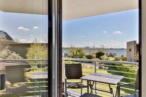 A balcony with a table and chairs, overlooking a body of water and greenery.