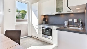 Una cocina moderna con armarios blancos, horno empotrado y un amplio ventanal que proporciona luz natural.