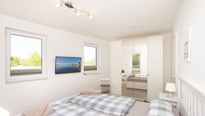 Un dormitorio con dos camas, un televisor y un amplio ventanal con vistas a árboles y un lago.