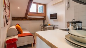 A compact kitchen with a dining area, a window with wooden beams, a red stool, and a TV mounted on the wall. - Rialto Rooftop Terrace Loft (Venice)
