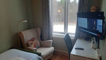A room with a bed, a chair, a desk with a computer, and a window with curtains.