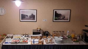 A breakfast buffet with various food items, a clock, and two framed pictures on the wall.