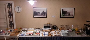 A breakfast buffet with various food items, a clock, and two framed pictures on the wall.