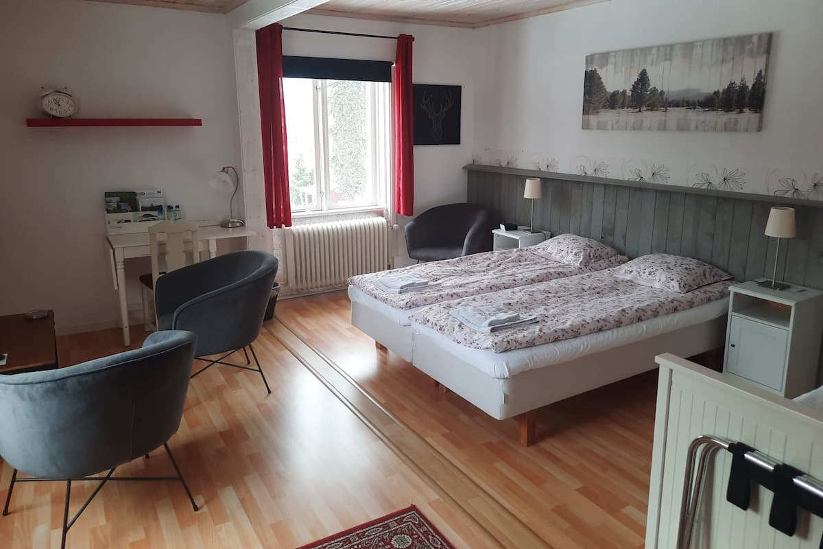 Een slaapkamer met een bed, een bureau, een stoel, een radiator en een raam met gordijnen.