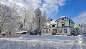 A large, two-story house with a snow-covered roof and surrounding trees.