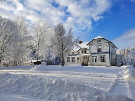 A large, two-story house with a snow-covered roof and surrounding trees.