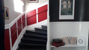 A staircase with red handrails and white walls, leading to a landing with a bench and a framed picture.