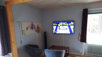 Una sala de estar con un televisor montado en la pared, un sillón azul, un banco de madera y un radiador.