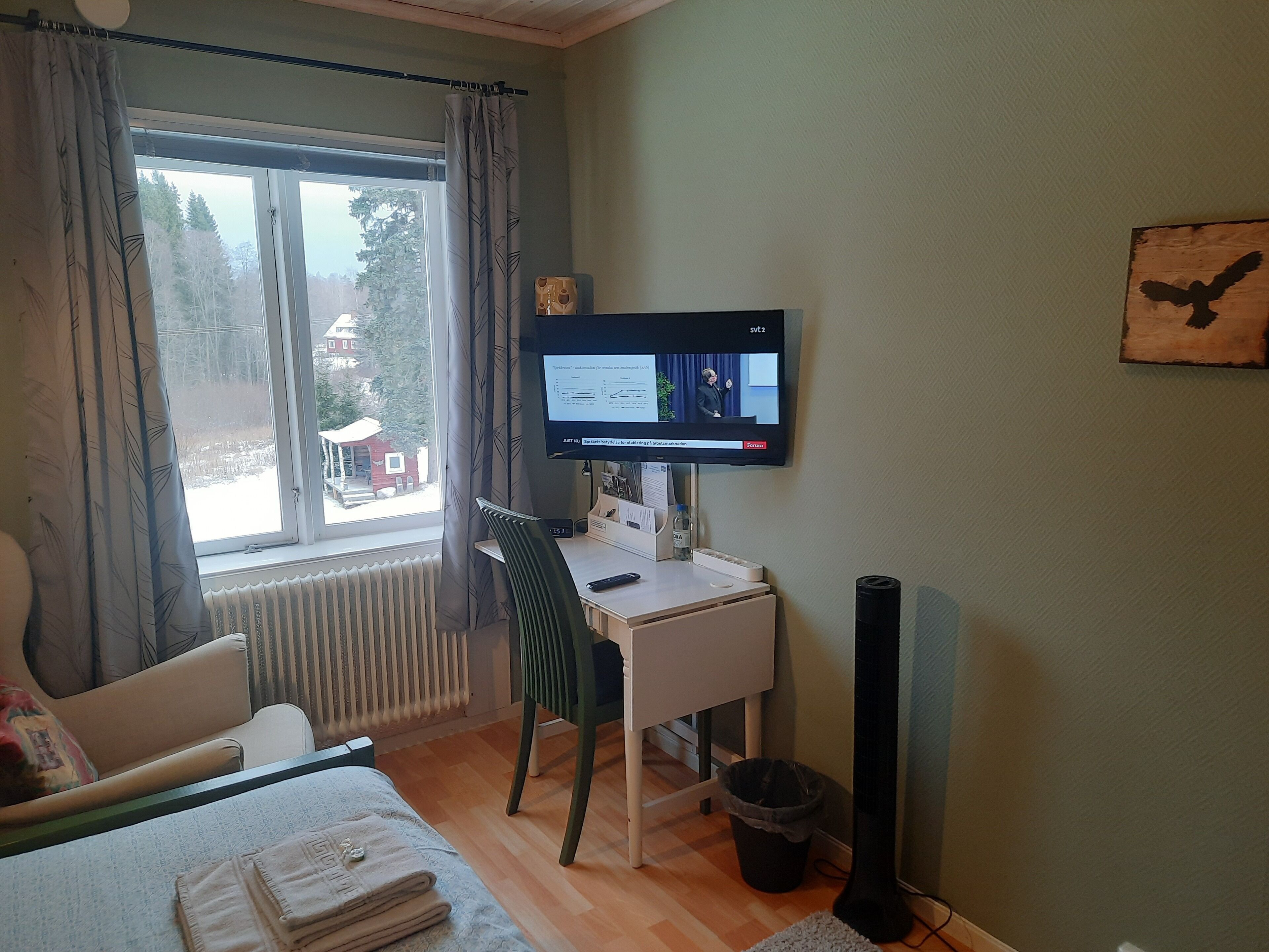 Een kamer met een bureau, stoel en een televisie waarop een nieuwskanaal wordt vertoond.