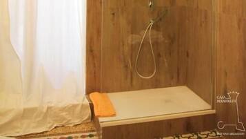 Ducha con paneles de madera, cabina de vidrio y un estante pequeño con una toalla.