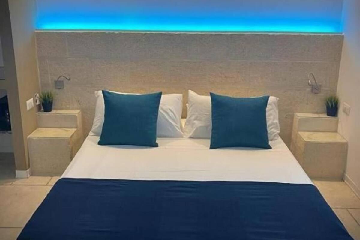 A modern bedroom with a large bed, two nightstands, and a blue-lit ceiling.