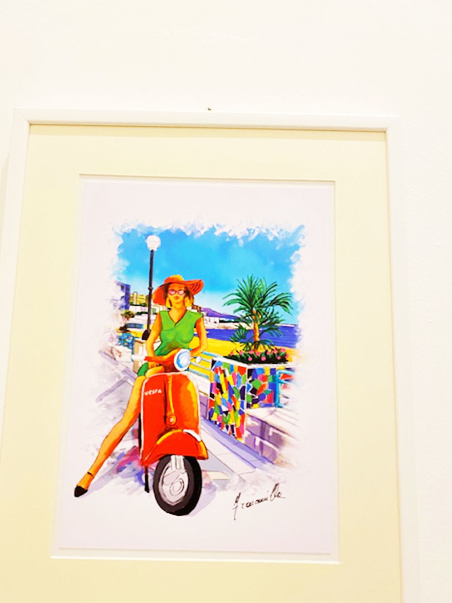 A framed artwork of a woman on a red scooter, with a signature at the bottom.