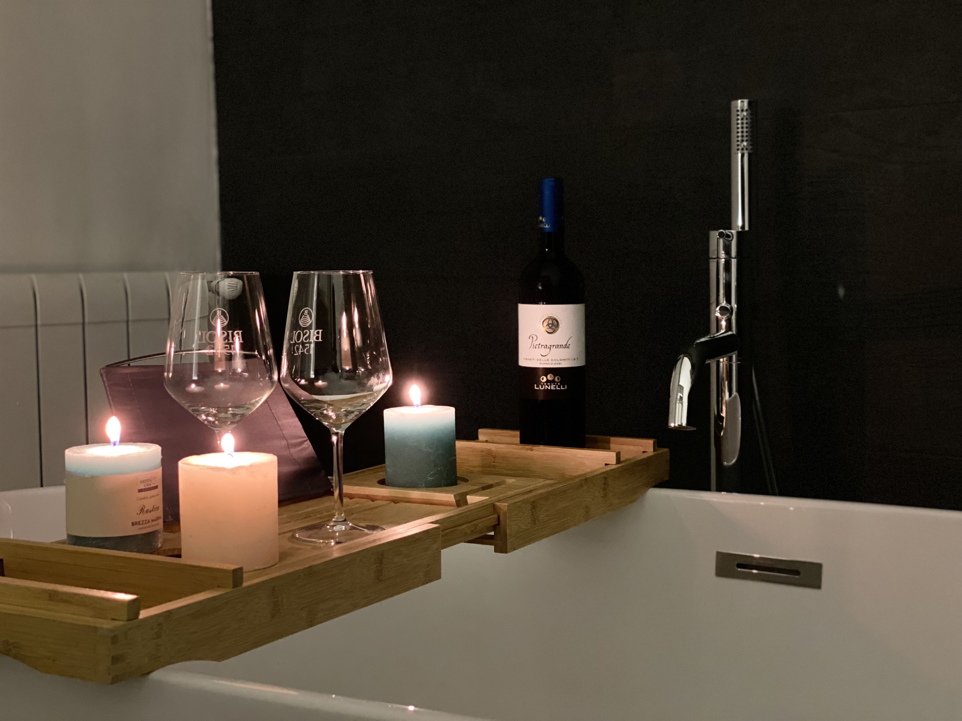 Une salle de bain avec un plateau en bois sur lequel sont posés deux verres à vin, une bougie et une bouteille de vin.