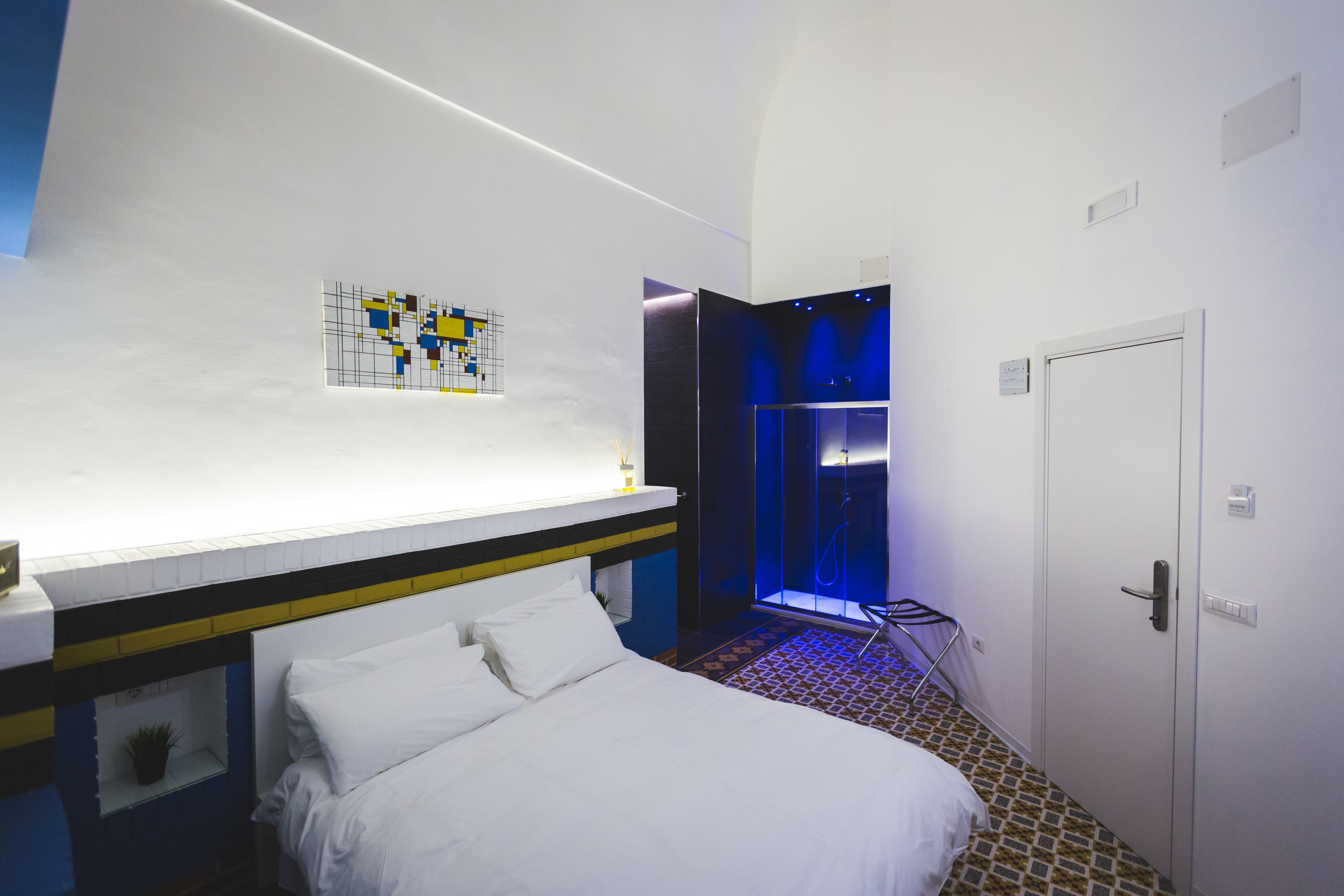 Hotellihuone, jossa on sänky, suihkutila ja seinälle kiinnitetty taideteos.