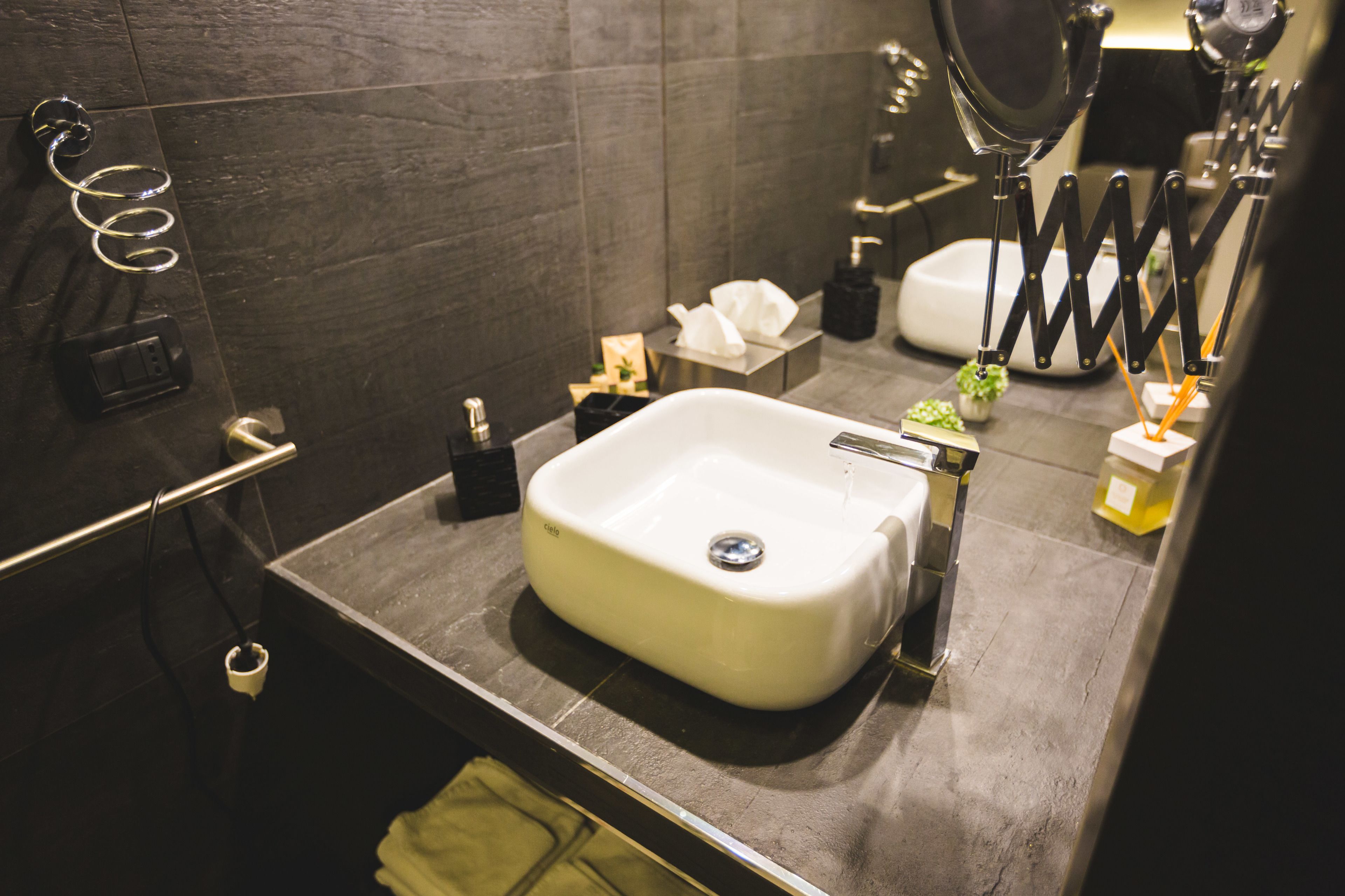 A modern bathroom with a white sink, dark tiles, a towel rack, and a mirror.