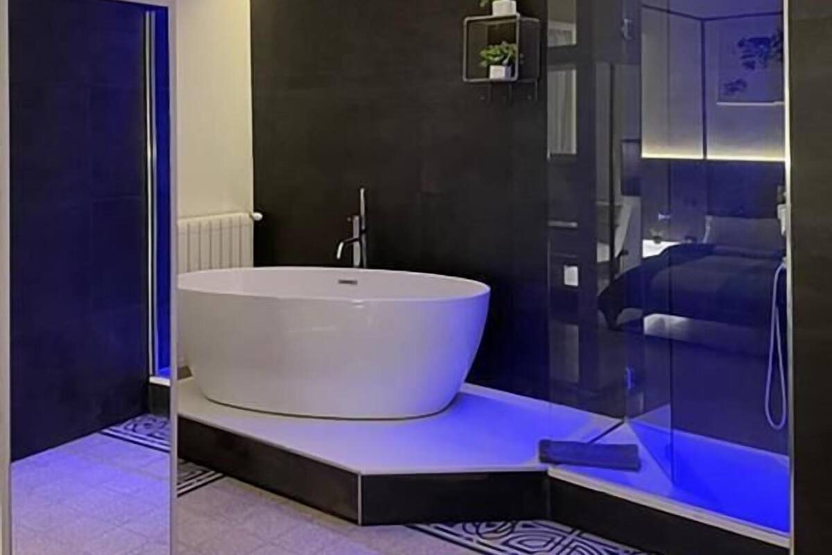 A modern bathroom with a freestanding bathtub, a glass shower enclosure, and a small shelf with a plant.