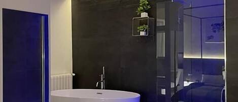 Un baño moderno con una bañera independiente, cabina de ducha con paredes de vidrio y un pequeño estante con una planta.