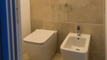 A bathroom with beige tiles, a toilet, and a bidet.