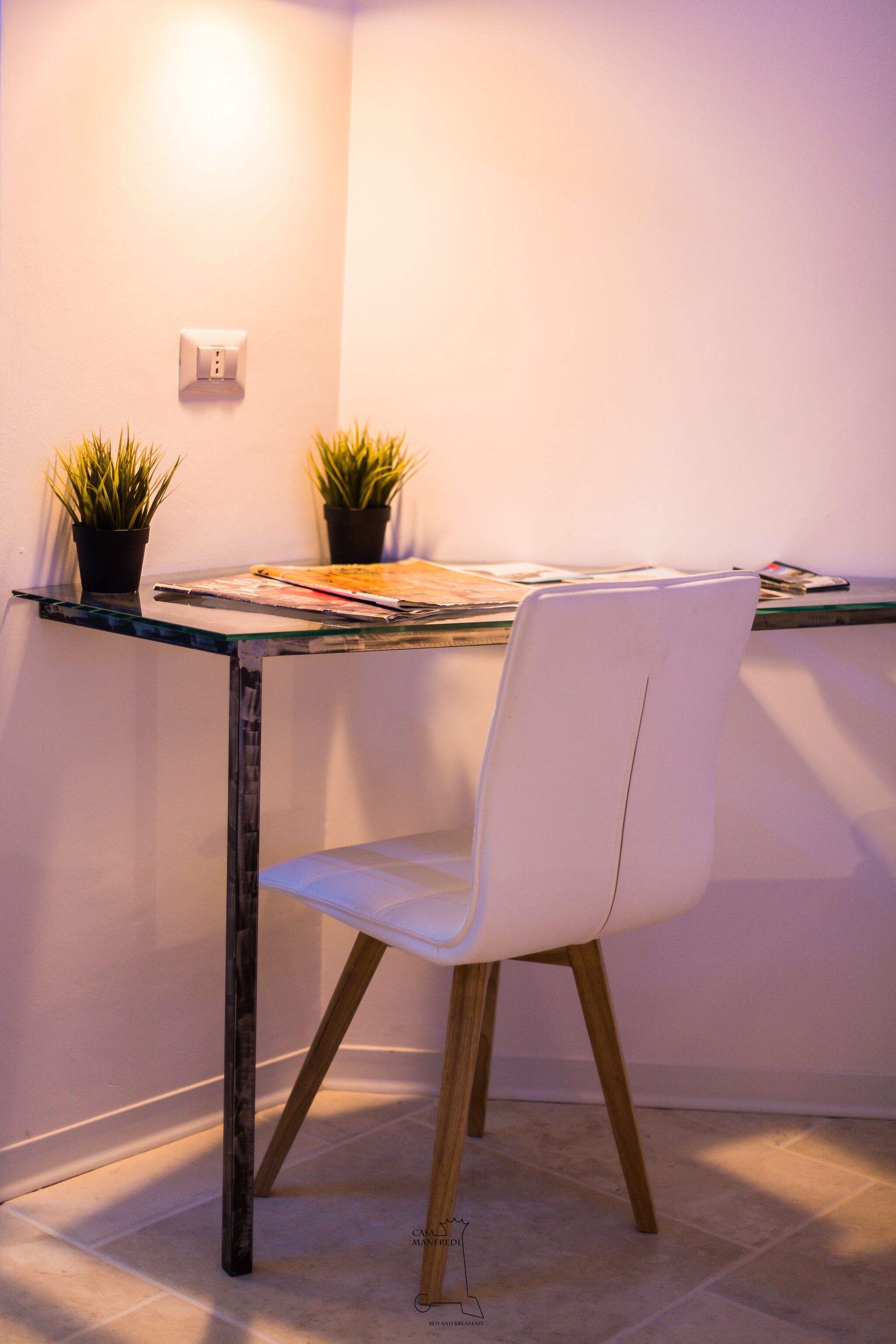 A modern workspace with a glass table, white chair, and two potted plants.