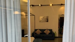 Een moderne hotelkamer met een glazen wand, een bank met gestreepte kussens, een blauw vloerkleed en een schilderij aan de muur.