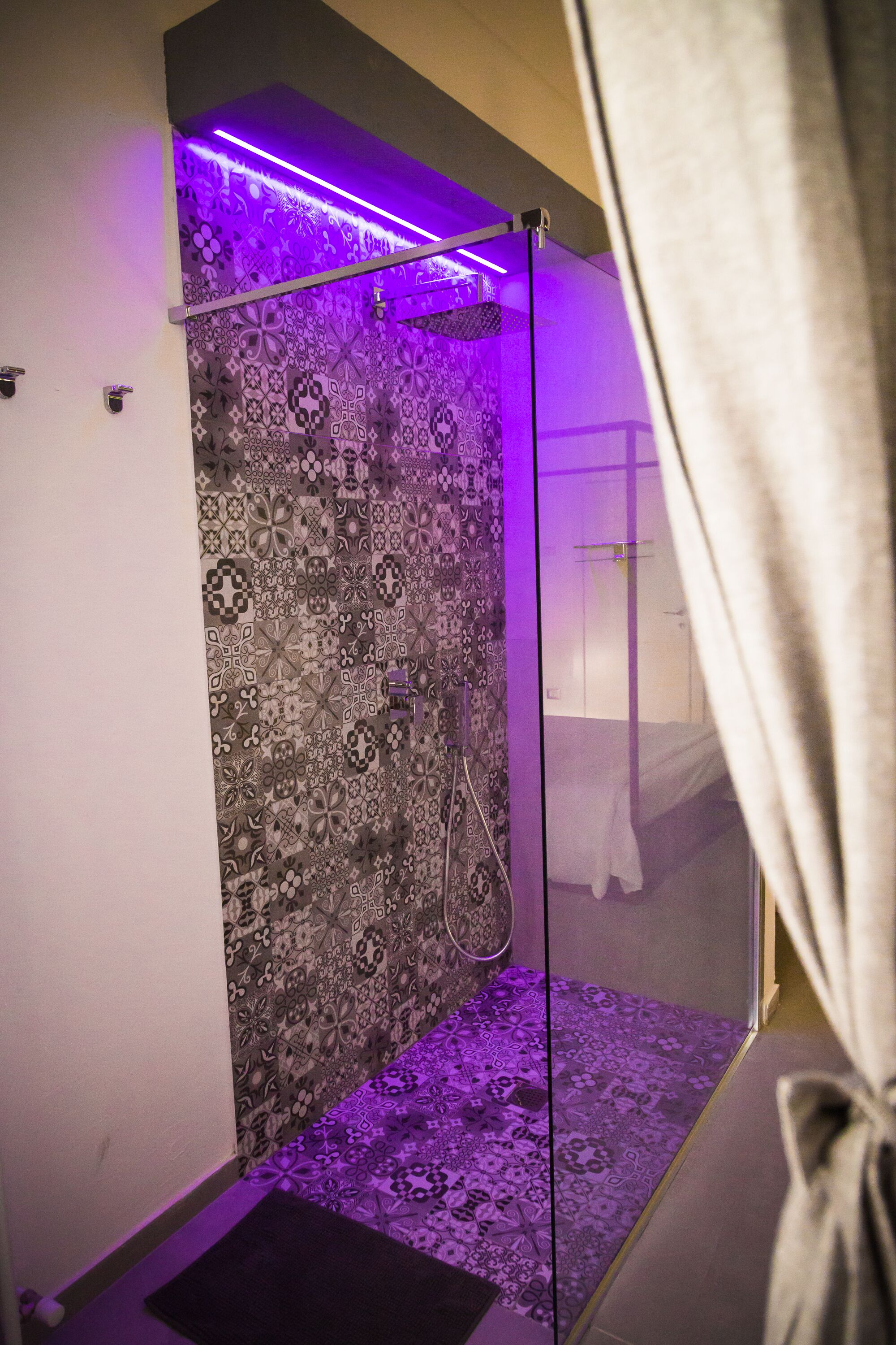 A shower with a patterned wall and purple lighting.