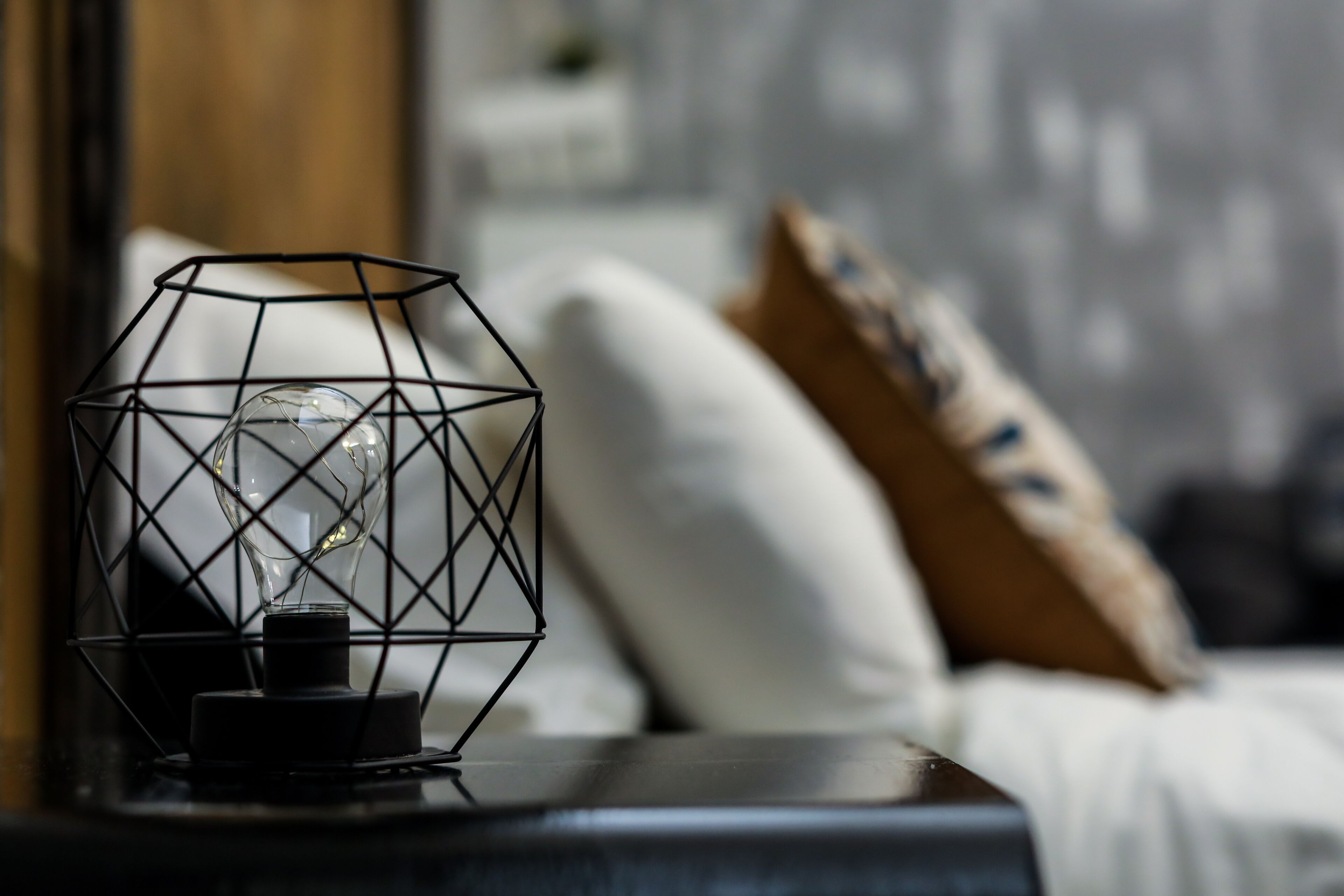 Uma luminária moderna com design geométrico sobre uma mesa de cabeceira em um quarto.