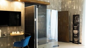 Een moderne hotelkamer met een flatscreen televisie, een blauwe stoel, een bank, een glazen douchecabine en een koffie plank.