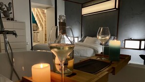 Een houten dienblad met een kaars, een fles en een glas witte wijn op een tafeltje in een hotelkamer.