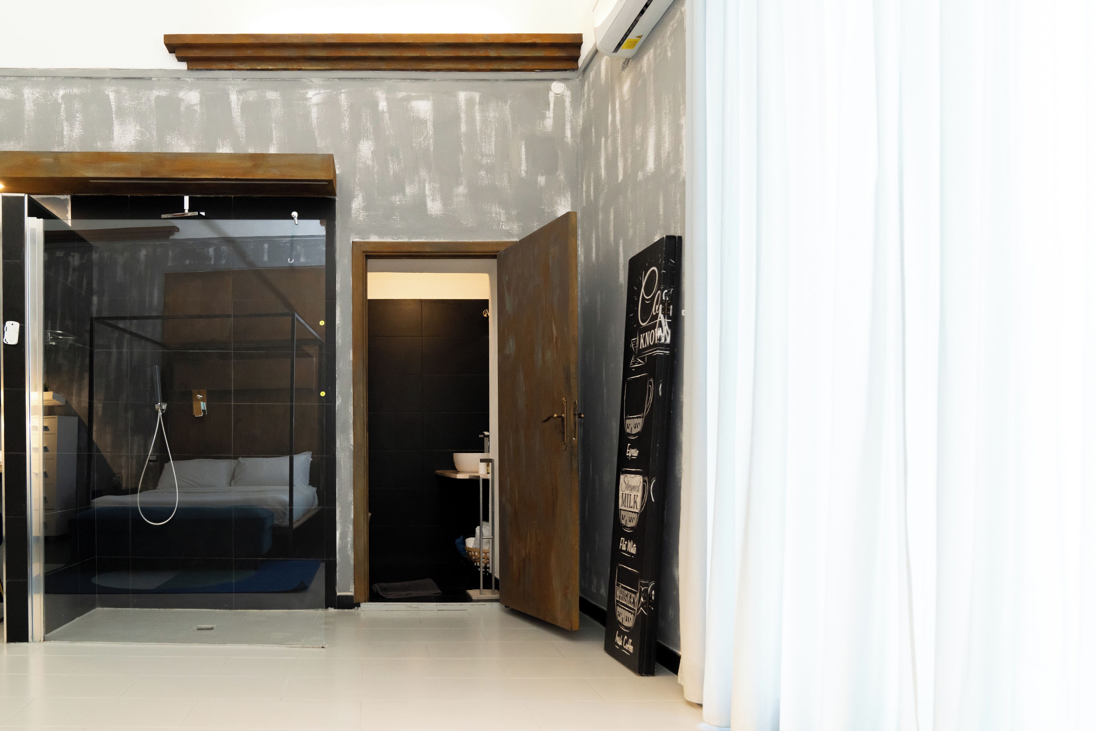 A hotel room with a glass shower enclosure, a wooden door, and a black cabinet with stickers.